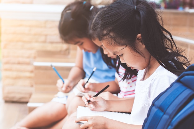 Groep Aziatische kinderen die een boek lezen en een notitieboekje samen schrijven