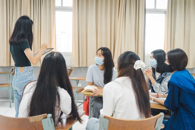 Groep Aziatische universiteitsstudenten dragen beschermend gezichtsmasker bespreken project in de klas