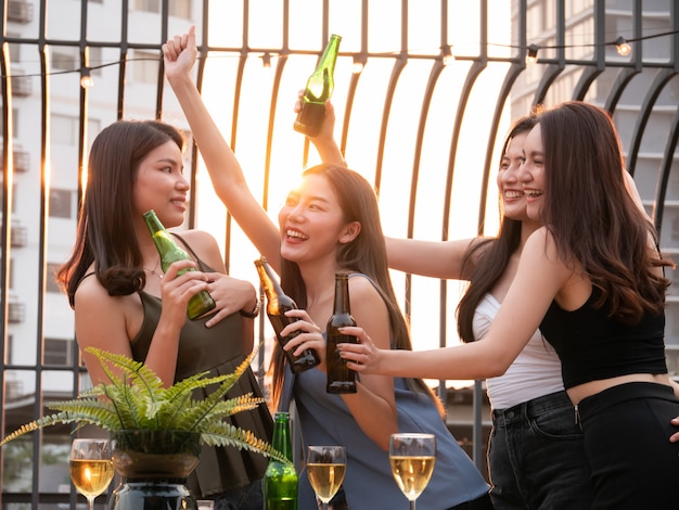 Groep Aziatische vriend die en bij terraspartij toejuichen drinken. Jongeren genieten en opknoping op het dak bij zonsondergang