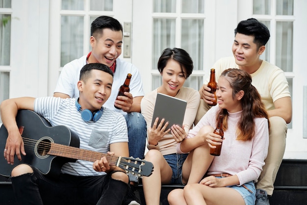 Groep Aziatische vrienden die bier drinken en liedjes zingen terwijl ze gitaar spelen tijdens een feestje