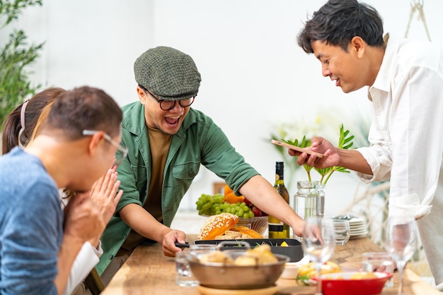 Groep Aziatische vrienden genieten van een dinerfeest en gebruiken mobiele telefoon fotografie eten op de eettafel thuis Gelukkige man en vrouw hereniging ontmoeting viering samen op vakantie vakantie