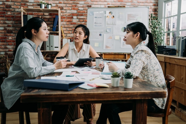 groep aziatische vrouwelijke collega's bespreken in vergaderruimte op creatief kantoor. twee dames luisteren geconcentreerd naar manager die praat en ideeën deelt in de bestuurskamer. klein start-up bedrijfsconcept