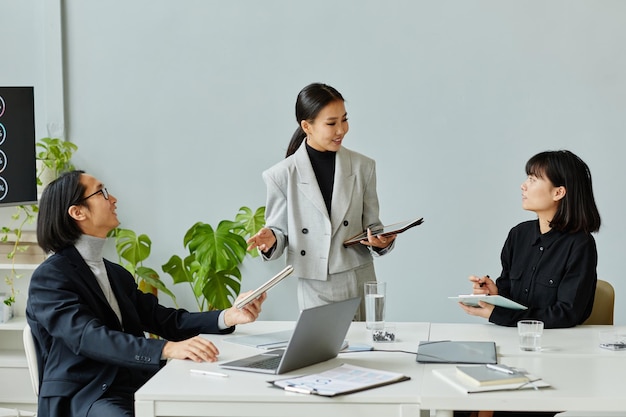 Groep Aziatische zakenmensen die op kantoor bijeenkomen, focussen op jonge vrouw die collega's instrueert