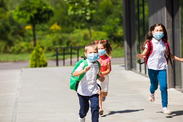 Groep basisschoolkinderen die naar de school rennen met beschermende maskers Beginnend onderwijsproces met nieuwe veiligheidsmaatregelregels