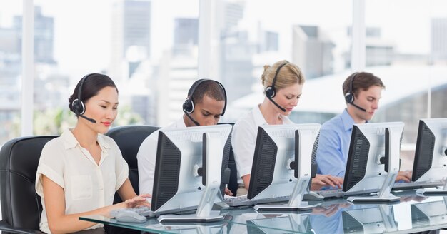 Groep bedrijfscollega&#39;s met hoofdtelefoons die computers met behulp van bij bureau