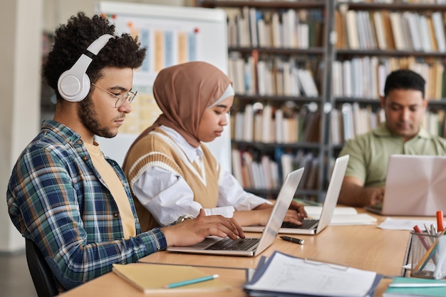 Groep buitenlandse studenten die computers gebruiken in hun studeerkamer terwijl ze aan tafel zitten in de bibliotheek