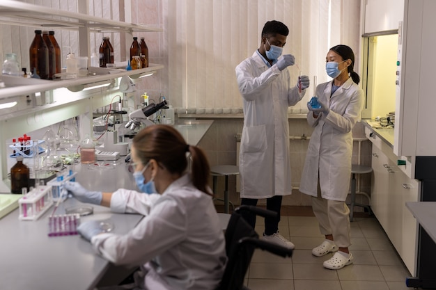 Groep chemici in witte jassen en maskers die monsters en reageerbuizen onderzoeken tijdens teamwerk in het laboratorium