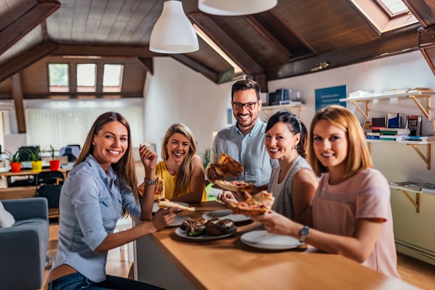 Groep collega&#39;s die pizza eten en camera bekijken.