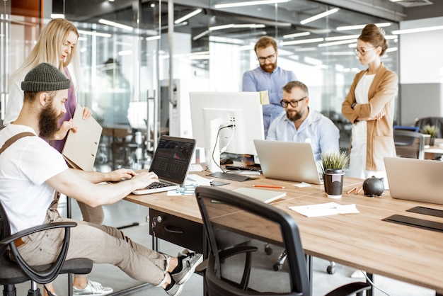 Groep diverse collega's die op de computers werken in de moderne kantoor- of coworking-ruimte, bebaarde hipster als programmeur die code schrijft