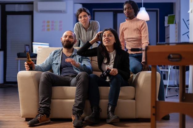 Groep diverse collega's die spel verliezen met vr-bril op console-tv terwijl ze joystickcontroller gebruiken. Multi-etnisch team dat plezier heeft met entertainment tijdens een happy indoor-viering