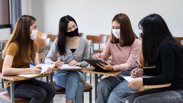 Groep diverse internationale studenten die beschermende maskers dragen en praten, een project bespreken, aan een bureau zitten in de klas op de universiteit