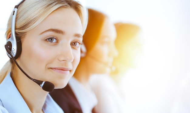 Groep diverse telefoonoperators aan het werk in zonnig kantoor. Knappe zakenvrouw met koptelefoon die klanten raadpleegt. Callcenter en mensen uit het bedrijfsleven concept.