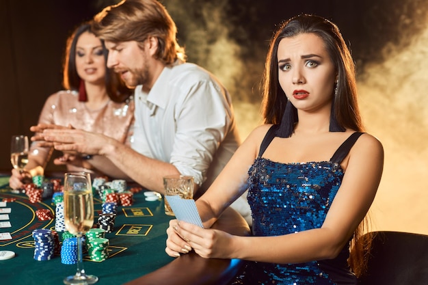 Groep elegante mensen die poker spelen in het gokhuis. Focus op een emotionele brunette in een blauwe glanzende jurk