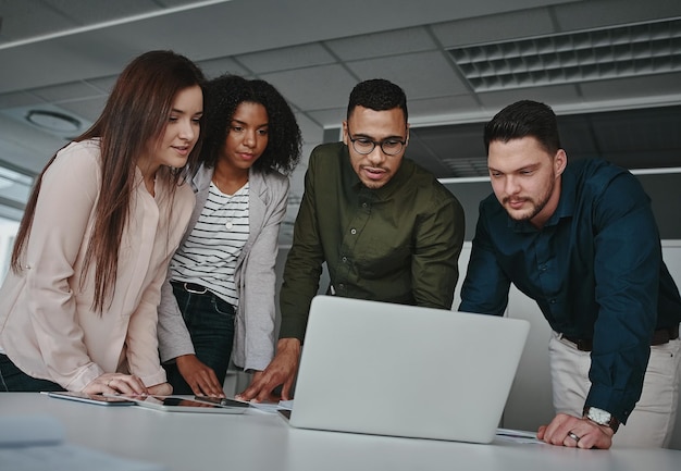 Groep geconcentreerd divers zakelijk team dat informatie bespreekt op het scherm van de laptop boven het bureau in het kantoor