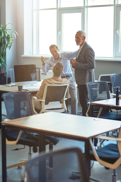 Groep gelukkige collega's die praten over iets en glimlachen terwijl ze samenwerken in