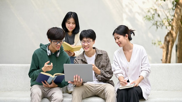 Groep gelukkige jonge Aziatische studenten die op een bank zitten en naar een laptopscherm kijken