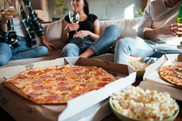 Foto groep gelukkige jongeren die pizza thuis eten, wijn drinken en bier op bank