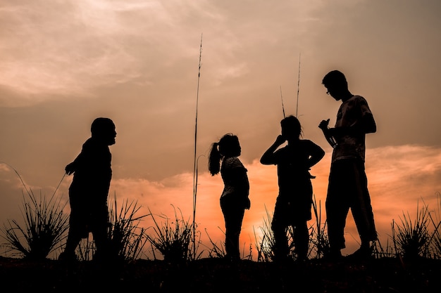 Groep gelukkige kinderen die op weide spelen bij zonsondergang, silhouet