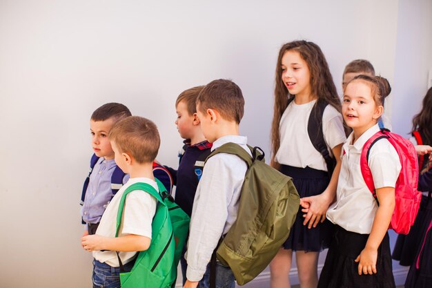 Groep gelukkige kleine schoolkinderen op school Kinderen in uniform met rugzakken in schoolgang