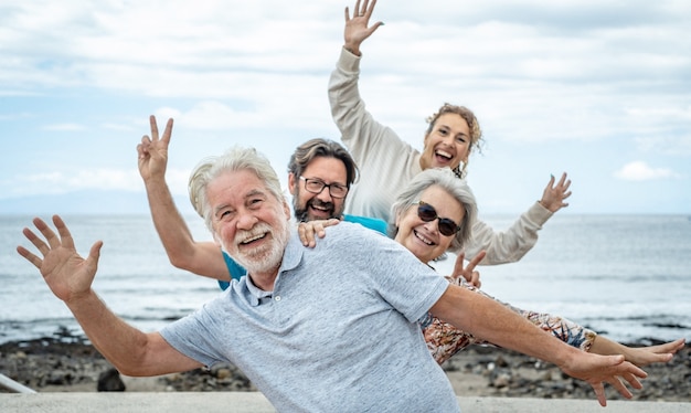 Groep gelukkige mensen die samen plezier hebben op zee, bewolkte hemel. Familie van meerdere generaties die positiviteit en vrijheid gebaren