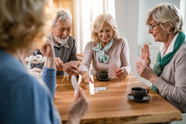 Groep gelukkige senioren speelkaarten aan de tafel in de woonkamer