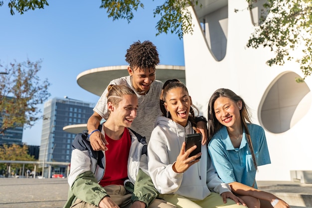 Groep gelukkige tienervrienden die naar de telefoon kijken en lachen in de stadsstraat