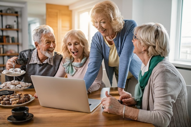 Groep gelukkige volwassen mensen die plezier hebben tijdens het surfen op het net op een computer thuis