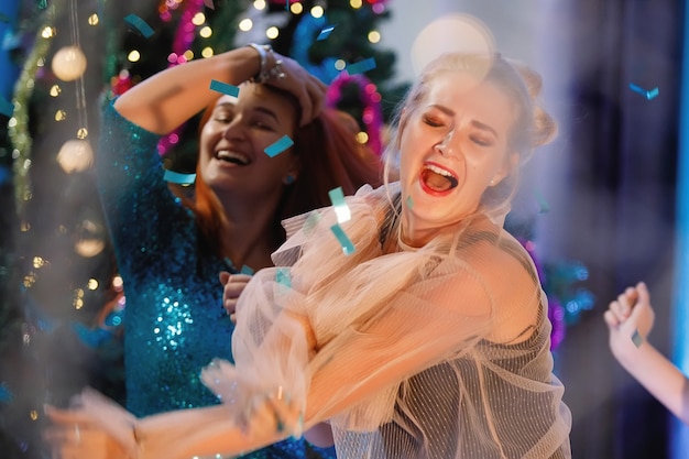 Groep gelukkige vrienden dansen in de buurt van de kerstboom. Vrouwen lachen, verheugen zich. Vintage filter voor ruis en graan, wazige lichten.