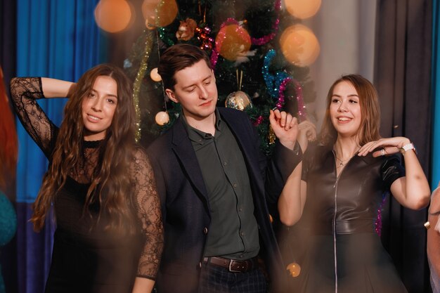 Groep gelukkige vrienden dansen in de buurt van de kerstboom. Vrouwen lachen, verheugen zich.