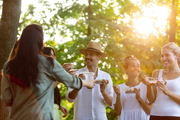 Groep gelukkige vrienden die bieren eten en drinken tijdens het barbecuediner op zonsondergangtijd