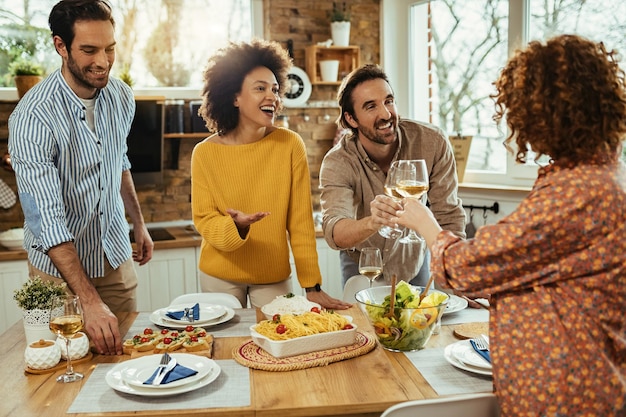 Groep gelukkige vrienden die plezier hebben tijdens het bereiden van de eettafel voor de lunch en roosteren met wijn