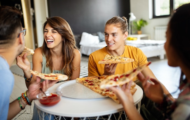 Groep gelukkige vrienden die thuis feesten, pizza eten en plezier hebben.