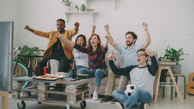 Groep gelukkige vrienden die thuis naar sportwedstrijden op tv kijken Ze zijn blij met de overwinning van hun favoriete team