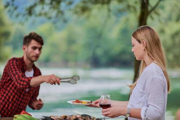 groep gelukkige vrienden hebben een picknick Frans etentje buiten tijdens de zomervakantie vakantie in de buurt van de rivier in de prachtige natuur
