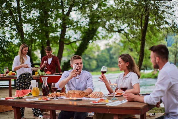 groep gelukkige vrienden hebben een picknick Frans etentje buiten tijdens de zomervakantie vakantie in de buurt van de rivier in de prachtige natuur