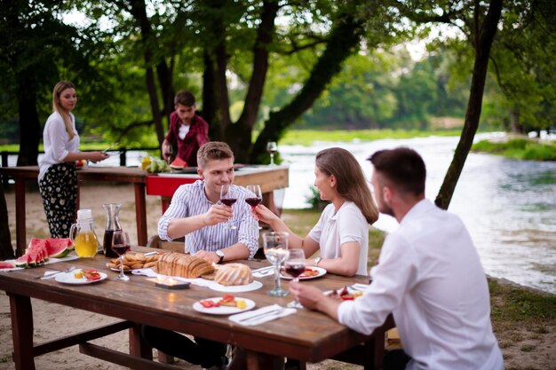 groep gelukkige vrienden hebben een picknick Frans etentje buiten tijdens de zomervakantie vakantie in de buurt van de rivier in de prachtige natuur