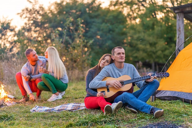 Groep gelukkige vrienden met gitaar, plezier buiten, in de buurt van vuur en toeristische tent. campingplezier gelukkig gezin