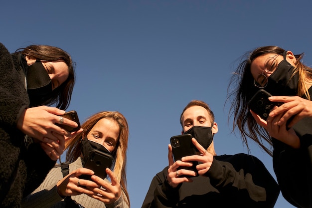 Groep gemaskerde vrienden die smartphones gebruiken