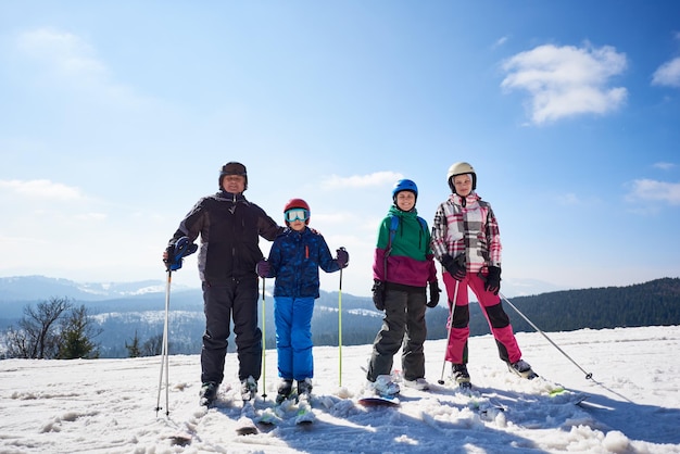 Groep glimlachende mensen op ski's en snowboard in diepe sneeuw op de achtergrond van blauwe lucht en bergen