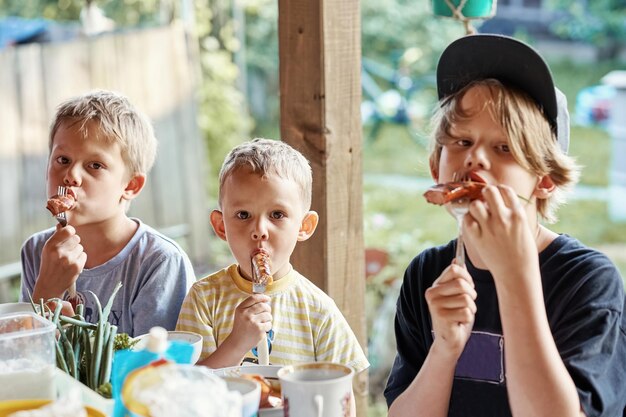 Foto groep hongerige broers eet heerlijke gegrilde worstjes zittend aan tafel op het terras in de zomer