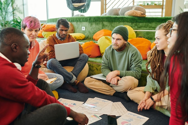 Groep interculturele financiële managers die brainstormen en documenten bespreken met grafieken en diagrammen tijdens een werkvergadering op de vloer