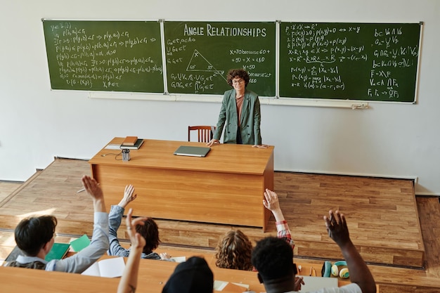 Groep interraciale studenten die handen opsteken om vragen aan leraar te stellen