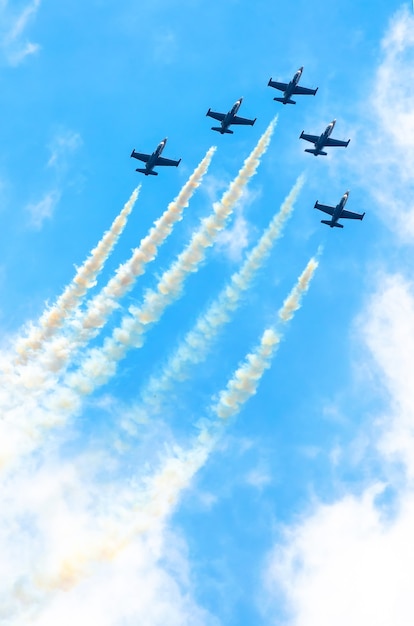 Groep jachtvliegtuigen vliegen omhoog met een rookspoor tegen een blauwe lucht met wolken.