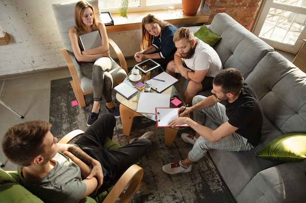 Groep jonge blanke kantoormedewerkers die bijeenkomen om nieuwe ideeën te bespreken. Creatieve bijeenkomst. Teamwerk en brainstormen. Mannen en vrouwen ontmoeten elkaar op kantoor om hun toekomstige werk te plannen. Bedrijfsconcept.