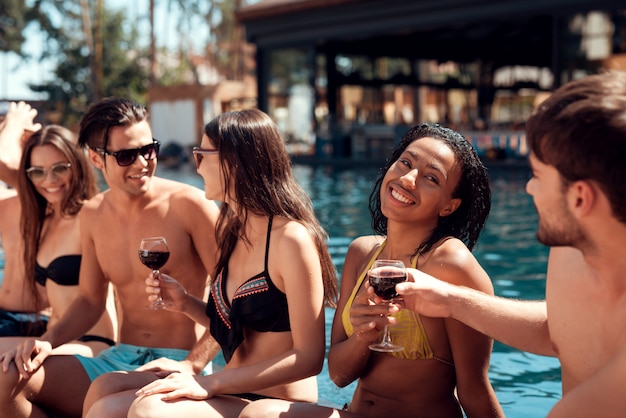 Groep jonge gelukkige mensen die bij Poolside samen zitten