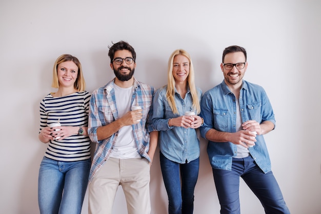 Groep jonge gelukkige mensen die zich tegen de muur bevinden en koffie houden om te gaan. Start bedrijfsconcept.