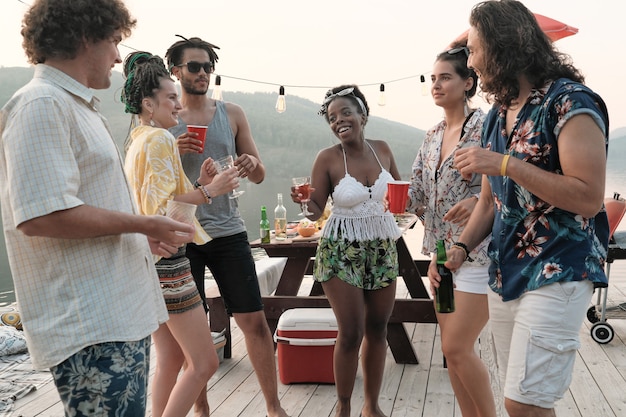 Groep jonge gelukkige mensen samen dansen en alcohol drinken tijdens het feest buiten