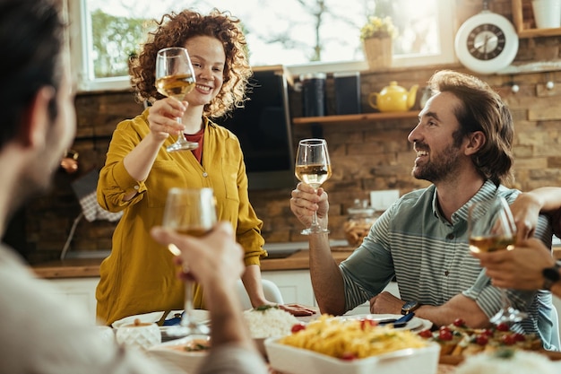 Groep jonge gelukkige vrienden die met wijn roosteren terwijl ze samen thuis lunchen