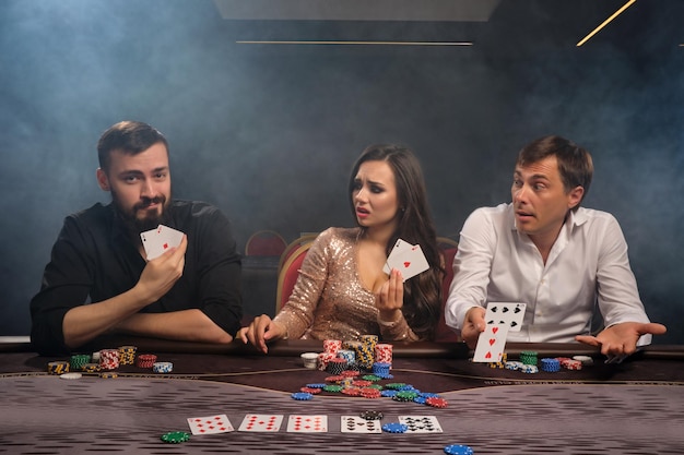 Groep jonge gelukkige vrienden spelen poker in casino in rook. Een van hen heeft gewonnen en de rest ziet er ontdaan uit. De jeugd maakt weddenschappen in afwachting van een grote overwinning. Gokken voor geld. spellen van voor