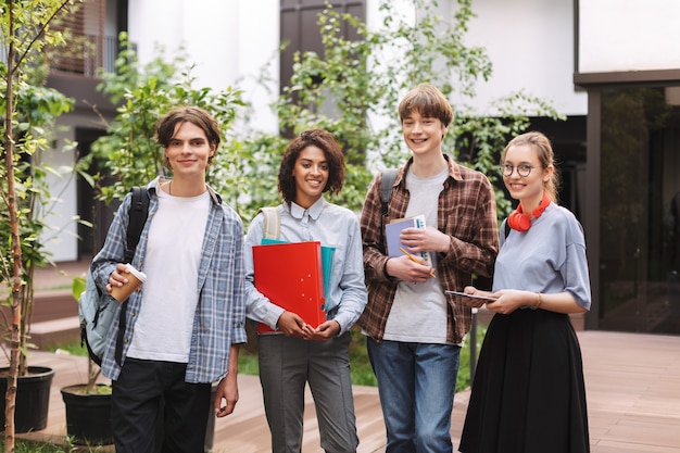 Groep jonge glimlachende studenten die zich met boeken en omslagen in handen en gelukkig bevinden